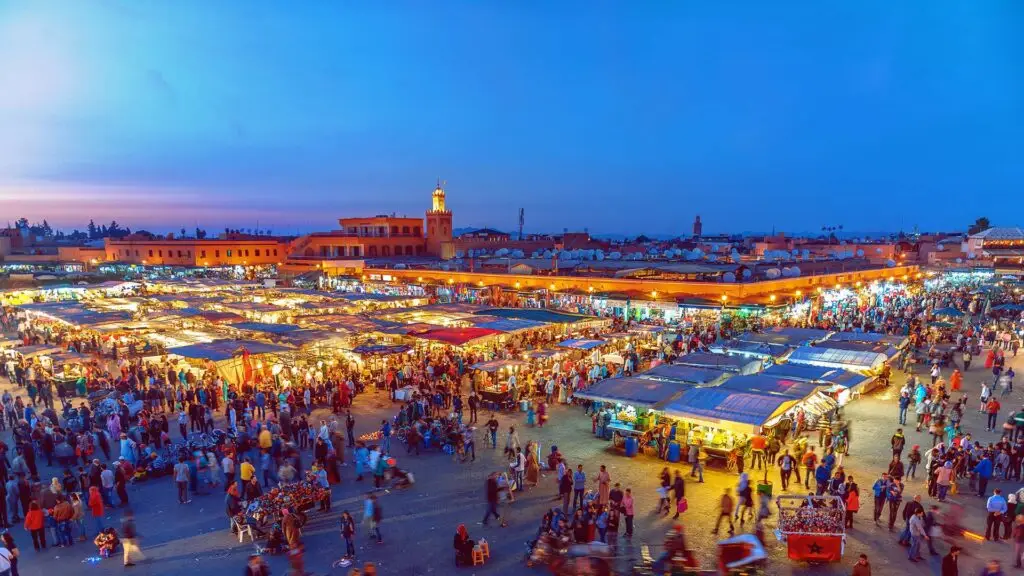 Bustling Jemaa el-Fnaa square in Marrakech with historic buildings, market stalls, and crowds, featured on Majesty Morocco Tours.